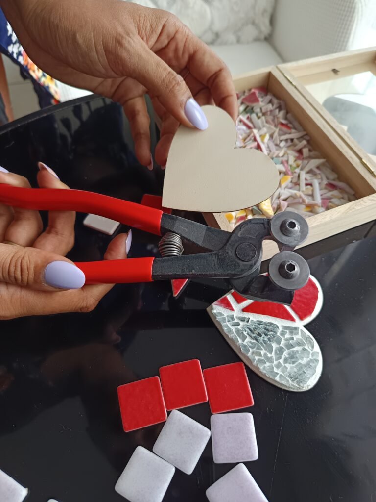 Un gros plan d’un détail de mosaïque en cours de création, avec des outils, des morceaux colorés, les mains en train de poser.